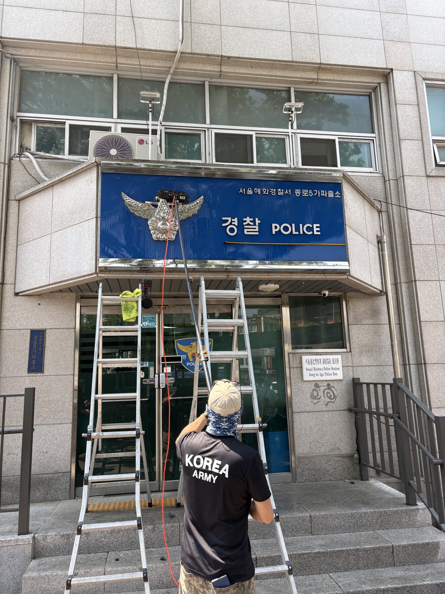사다리와 세척 장대로 건물 간판을 청소하는 클린덕 작업자